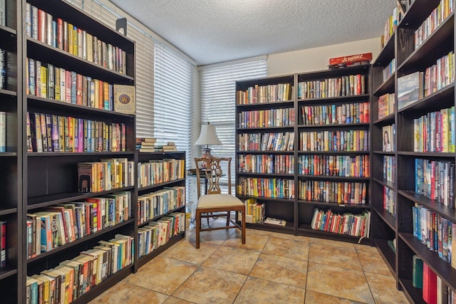 sitting room featuring tile patterned floors, wall of books, and a textured ceiling