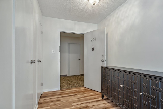 hallway with a textured ceiling and light wood finished floors