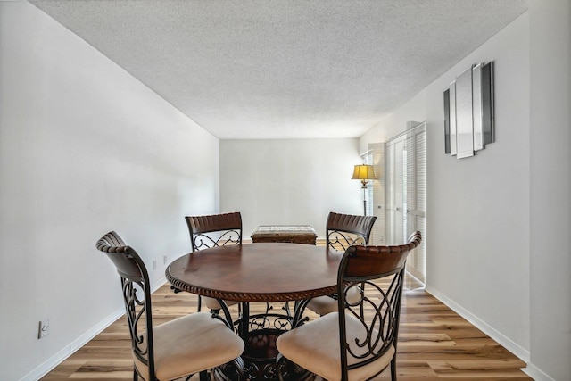 dining space featuring light wood-style flooring, a textured ceiling, and baseboards