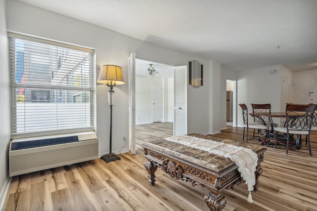 bedroom with freestanding refrigerator, a textured ceiling, light wood-type flooring, and a wall unit AC