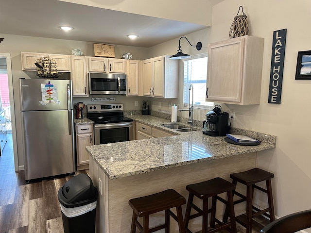 kitchen with a kitchen bar, stainless steel appliances, light stone counters, kitchen peninsula, and dark hardwood / wood-style floors