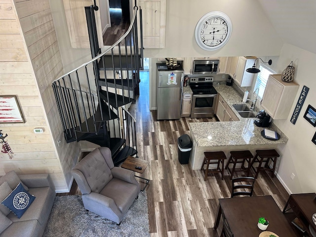 kitchen featuring high vaulted ceiling, wooden walls, stainless steel appliances, sink, and hardwood / wood-style flooring