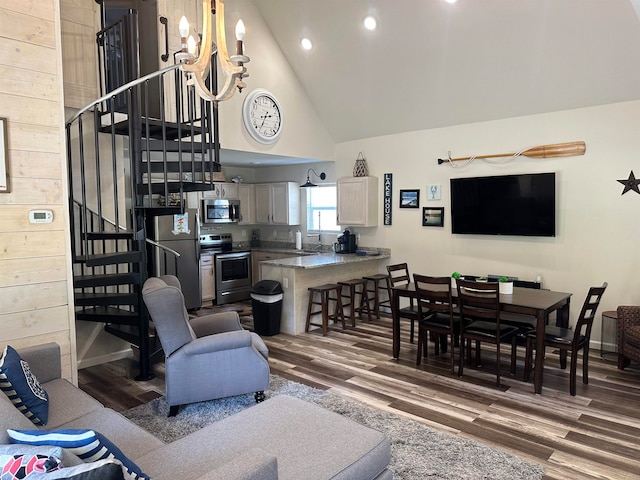 living room with high vaulted ceiling, an inviting chandelier, wooden walls, and dark wood-type flooring