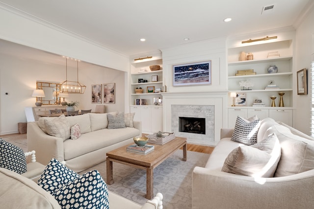 living room with recessed lighting, a fireplace with flush hearth, visible vents, built in features, and crown molding