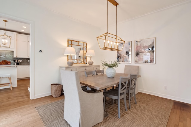 dining space featuring baseboards, light wood finished floors, crown molding, and an inviting chandelier