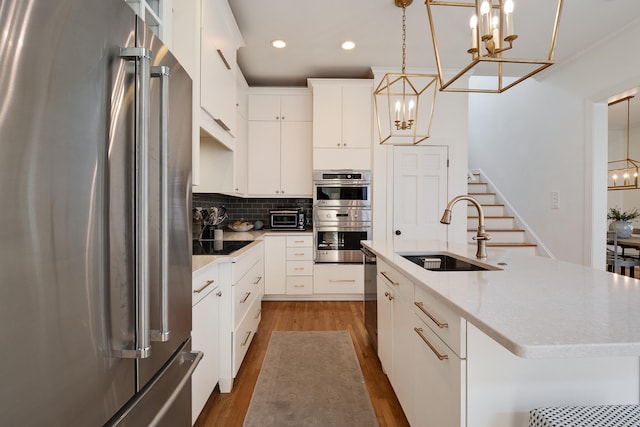 kitchen featuring tasteful backsplash, wood finished floors, a sink, stainless steel appliances, and a notable chandelier