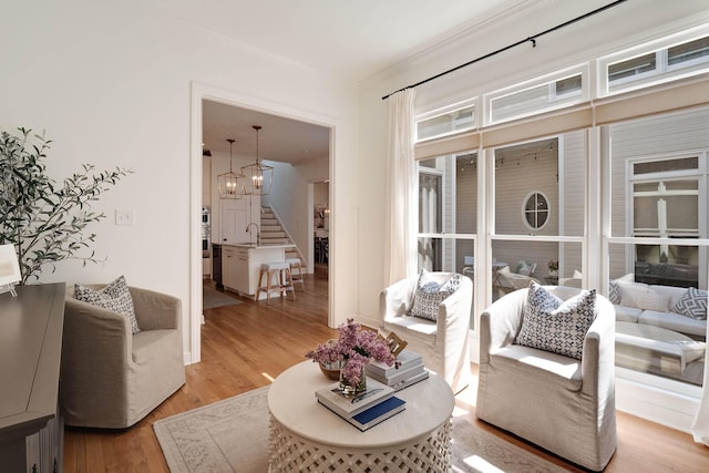 living room with light wood-style flooring, stairs, a chandelier, and crown molding