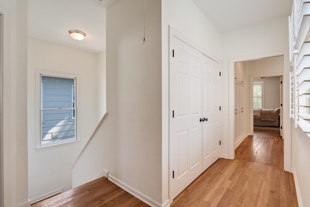 corridor with light wood-style floors, baseboards, and an upstairs landing