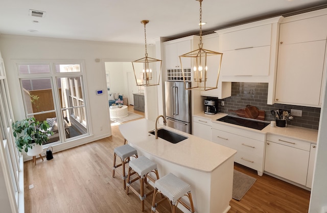 kitchen with black electric cooktop, a sink, visible vents, high end fridge, and light wood-type flooring