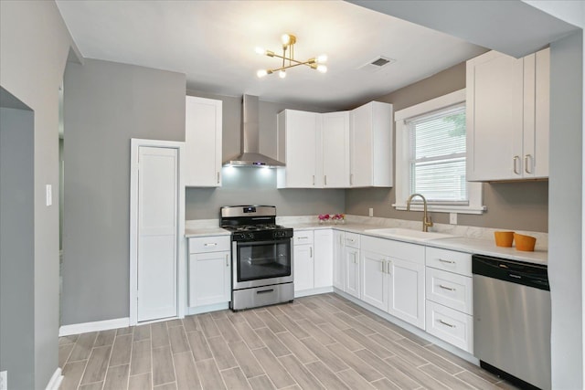 kitchen with white cabinets, stainless steel appliances, a notable chandelier, sink, and wall chimney exhaust hood