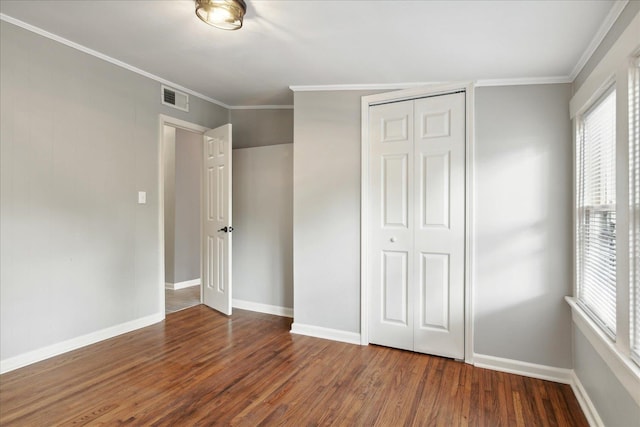 unfurnished bedroom with a closet, dark hardwood / wood-style flooring, and crown molding