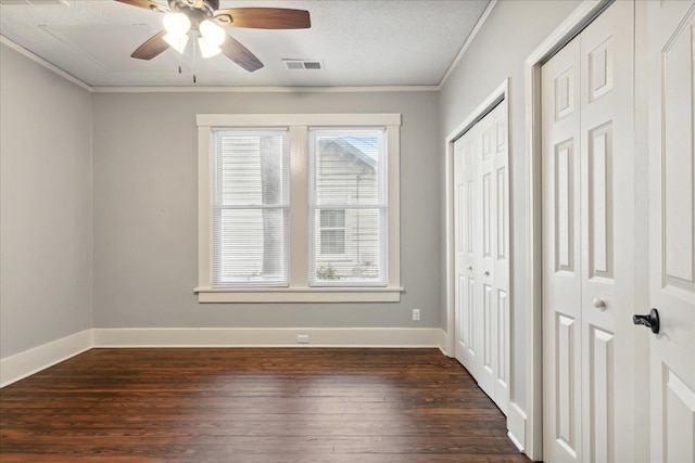 unfurnished bedroom with two closets, crown molding, dark hardwood / wood-style floors, ceiling fan, and a textured ceiling