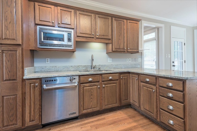 kitchen with a peninsula, ornamental molding, a sink, light wood-style floors, and appliances with stainless steel finishes