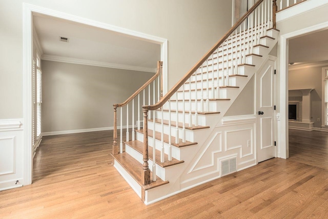 stairway with visible vents, wood finished floors, baseboards, and ornamental molding