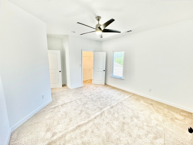 unfurnished bedroom with light carpet, a closet, ceiling fan, and a walk in closet