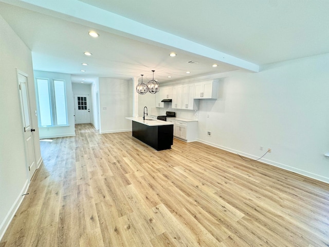 unfurnished living room with an inviting chandelier, beamed ceiling, sink, and light hardwood / wood-style flooring