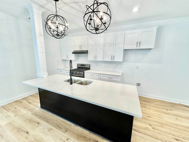 kitchen with hanging light fixtures, white cabinetry, light wood-type flooring, stainless steel range with gas stovetop, and a notable chandelier