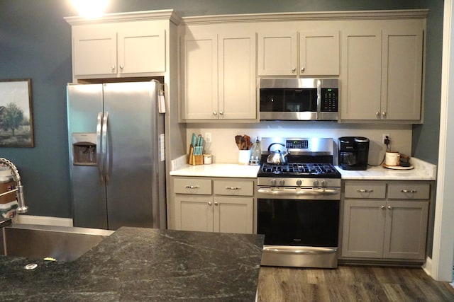 kitchen with sink, dark wood-type flooring, dark stone counters, and appliances with stainless steel finishes