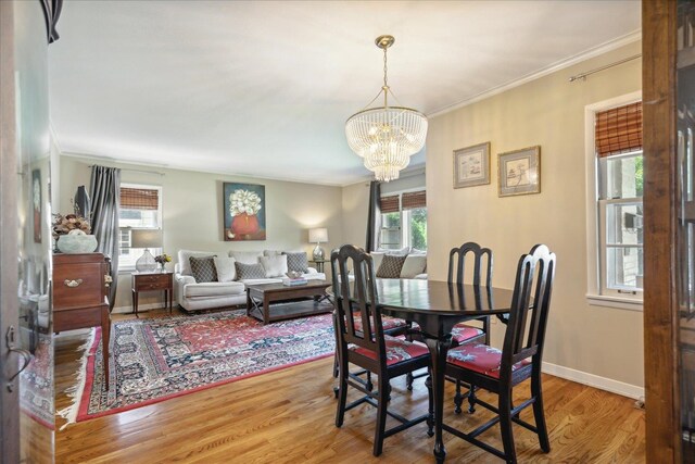 dining area with light wood-type flooring, crown molding, and a notable chandelier