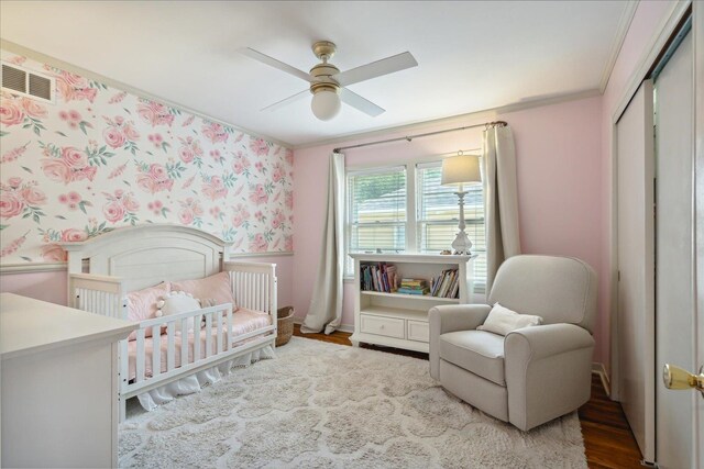 bedroom featuring a closet, wood-type flooring, ceiling fan, a nursery area, and ornamental molding