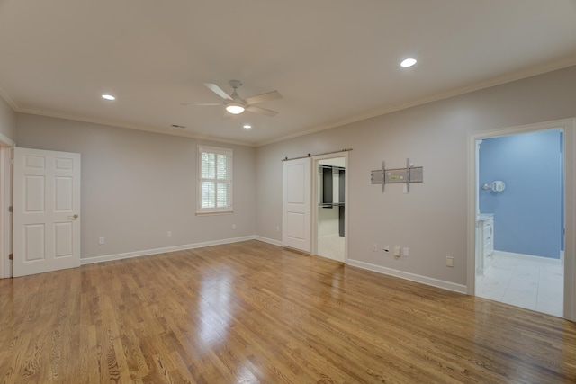 spare room featuring ceiling fan, a barn door, light hardwood / wood-style floors, and ornamental molding