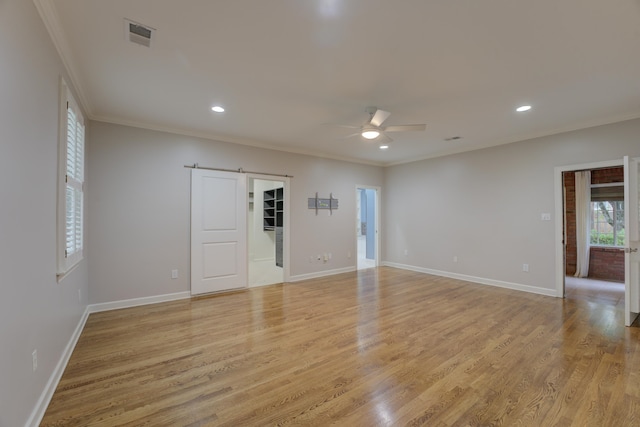 unfurnished room featuring a barn door, light hardwood / wood-style floors, ceiling fan, and ornamental molding