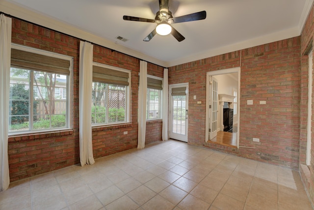 tiled empty room with ceiling fan, a healthy amount of sunlight, and brick wall