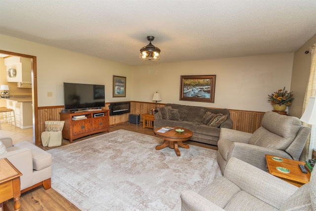 living room featuring light wood-type flooring, wood walls, and a textured ceiling