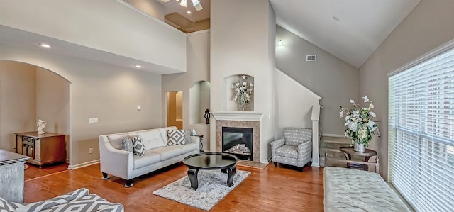 living room featuring high vaulted ceiling, a fireplace, arched walkways, and wood finished floors