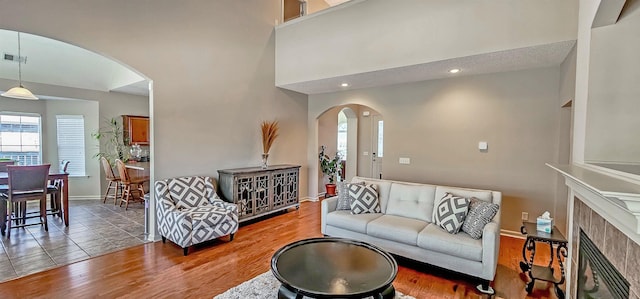 living room with arched walkways, a fireplace, wood finished floors, a towering ceiling, and baseboards