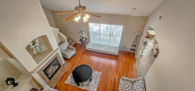 living area with ceiling fan, a tile fireplace, wood finished floors, visible vents, and stairway