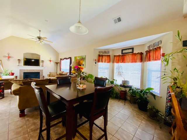 tiled dining space with lofted ceiling, ceiling fan, and a tiled fireplace