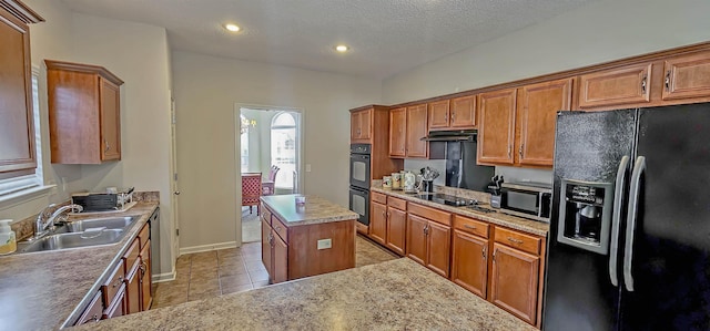 kitchen with light tile patterned floors, brown cabinetry, a sink, under cabinet range hood, and black appliances