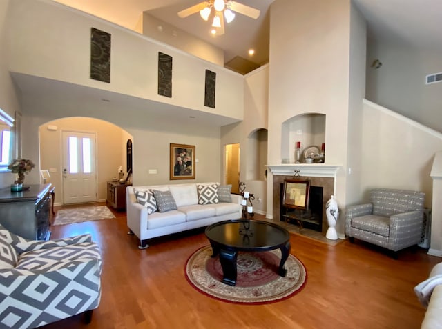 living room featuring dark wood-type flooring, ceiling fan, and a high ceiling