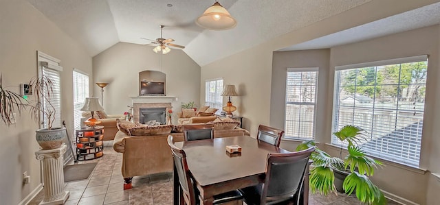 dining room featuring lofted ceiling, light tile patterned floors, a textured ceiling, a ceiling fan, and a glass covered fireplace