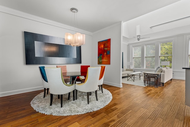 dining space with baseboards, wood finished floors, crown molding, and ceiling fan with notable chandelier