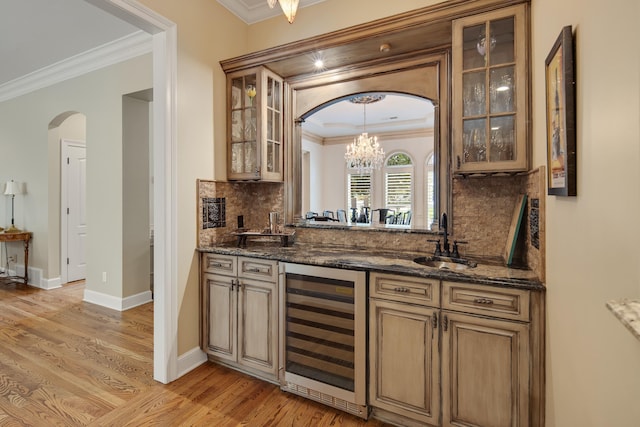 bar with wine cooler, arched walkways, indoor wet bar, light wood finished floors, and a sink