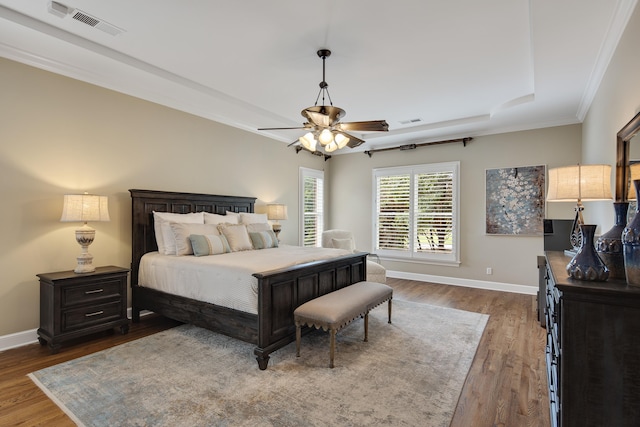 bedroom with a tray ceiling, dark wood-style flooring, visible vents, and baseboards