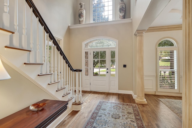 foyer entrance featuring a high ceiling, wood finished floors, decorative columns, and baseboards