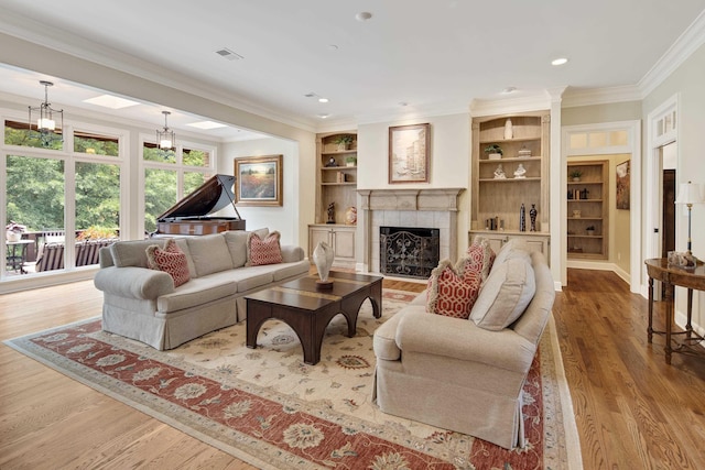 living room featuring visible vents, a tiled fireplace, wood finished floors, crown molding, and built in shelves