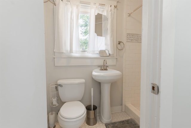 bathroom with toilet, a tile shower, and tile patterned floors