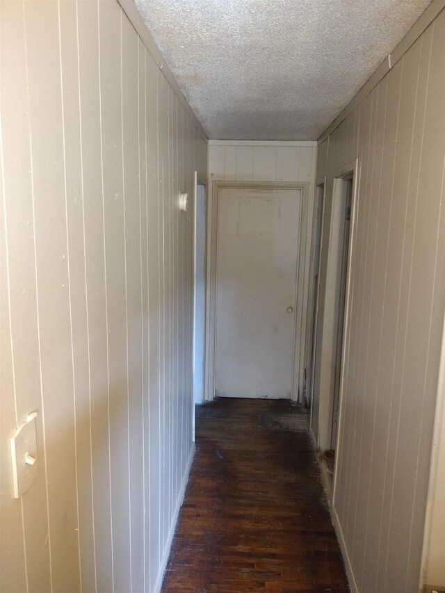 hall featuring a textured ceiling, dark hardwood / wood-style floors, and wooden walls