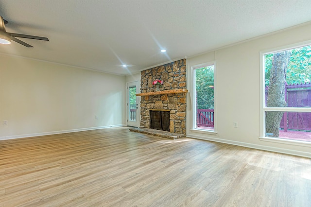 unfurnished living room featuring a textured ceiling, a stone fireplace, ornamental molding, ceiling fan, and light wood-type flooring