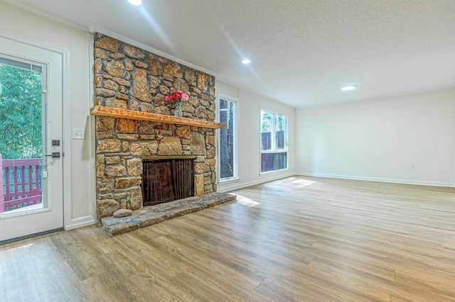 unfurnished living room featuring ornamental molding, a textured ceiling, wood-type flooring, and a stone fireplace