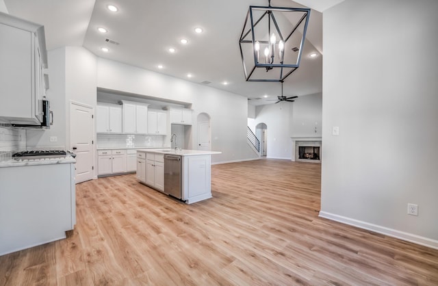 kitchen featuring open floor plan, dishwasher, an island with sink, a fireplace, and arched walkways