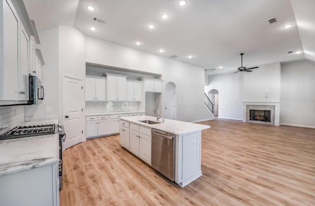 kitchen featuring lofted ceiling, a fireplace, arched walkways, a sink, and stainless steel appliances