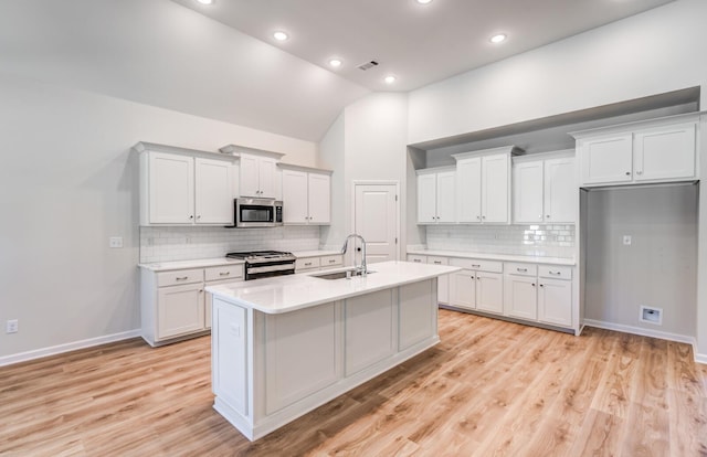 kitchen featuring visible vents, an island with sink, a sink, stainless steel appliances, and light countertops