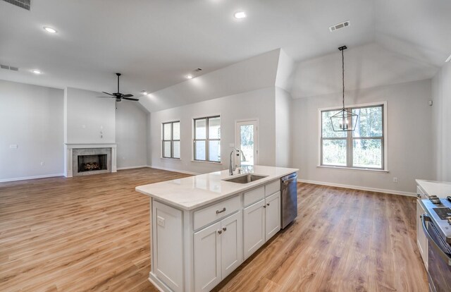 kitchen with white cabinets, vaulted ceiling, ceiling fan with notable chandelier, sink, and an island with sink