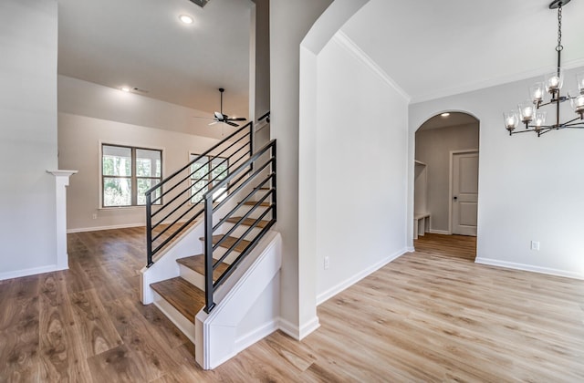 stairway with wood finished floors, baseboards, arched walkways, ornamental molding, and ceiling fan with notable chandelier