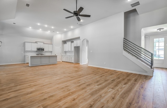 unfurnished living room featuring visible vents, light wood-type flooring, stairs, arched walkways, and a ceiling fan